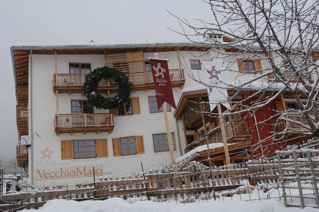 Esterno dell'hotel sotto la neve con insegna Relais Vecchio Maso e bandiere rosse
