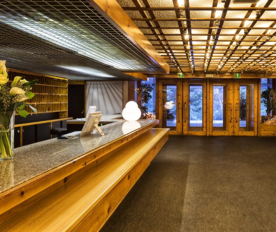 Reception dell'hotel con bancone in legno e granito, soffitto luminoso e ingresso vetrato
