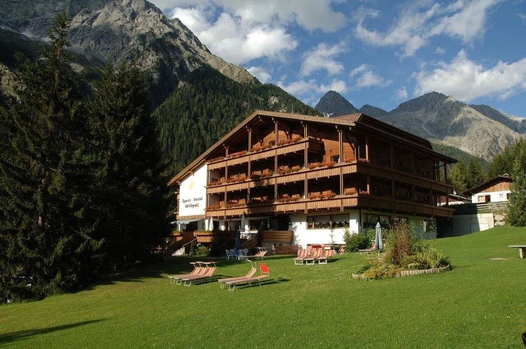 Hotel in legno con prato verde e sdraio circondato dalle montagne in estate