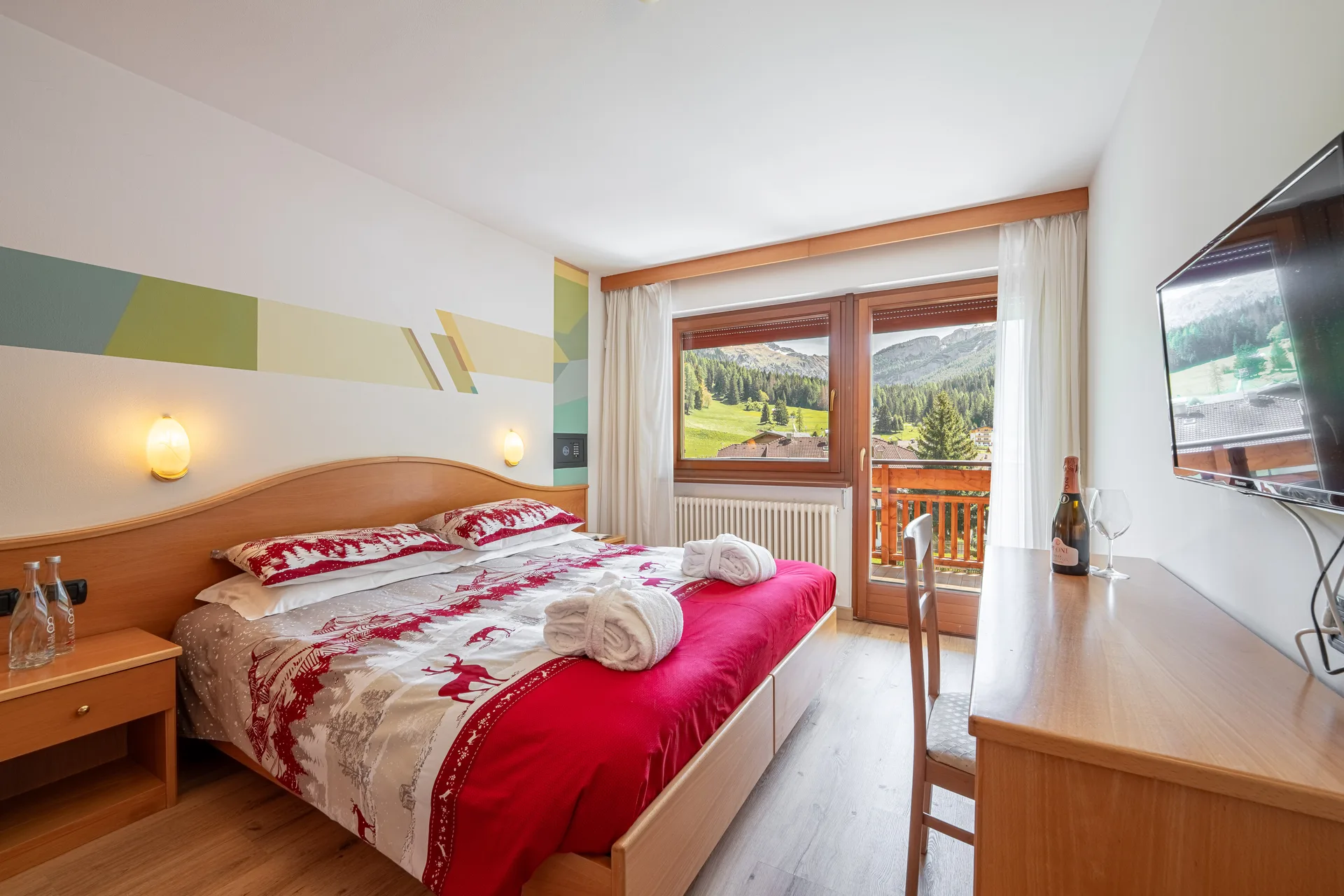Camera matrimoniale con vista sulle Dolomiti e sui prati verdi, arredo in legno, TV e balcone