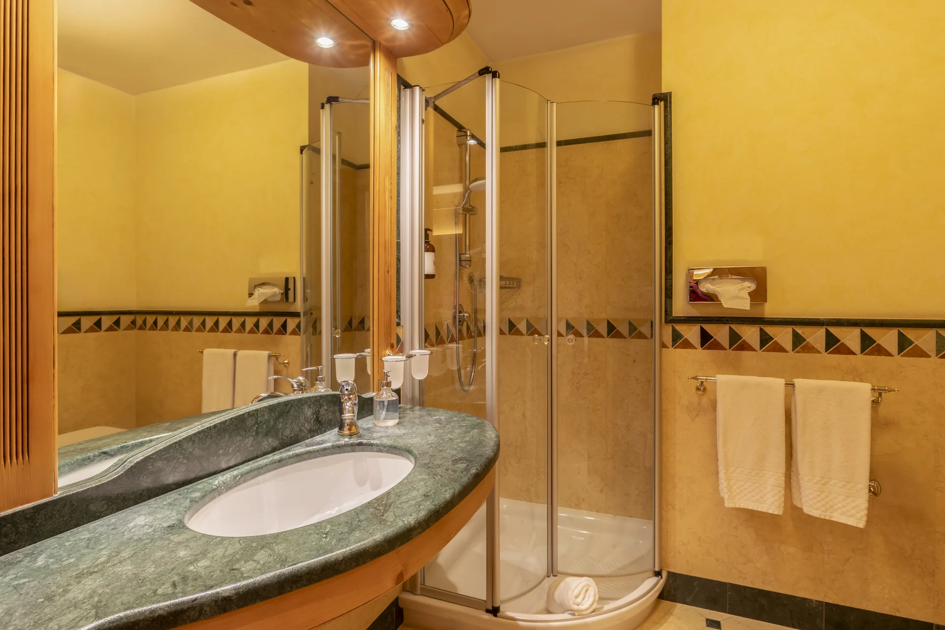 Bagno con lavabo in marmo verde, doccia in vetro e pareti gialle con decorazioni a mosaico