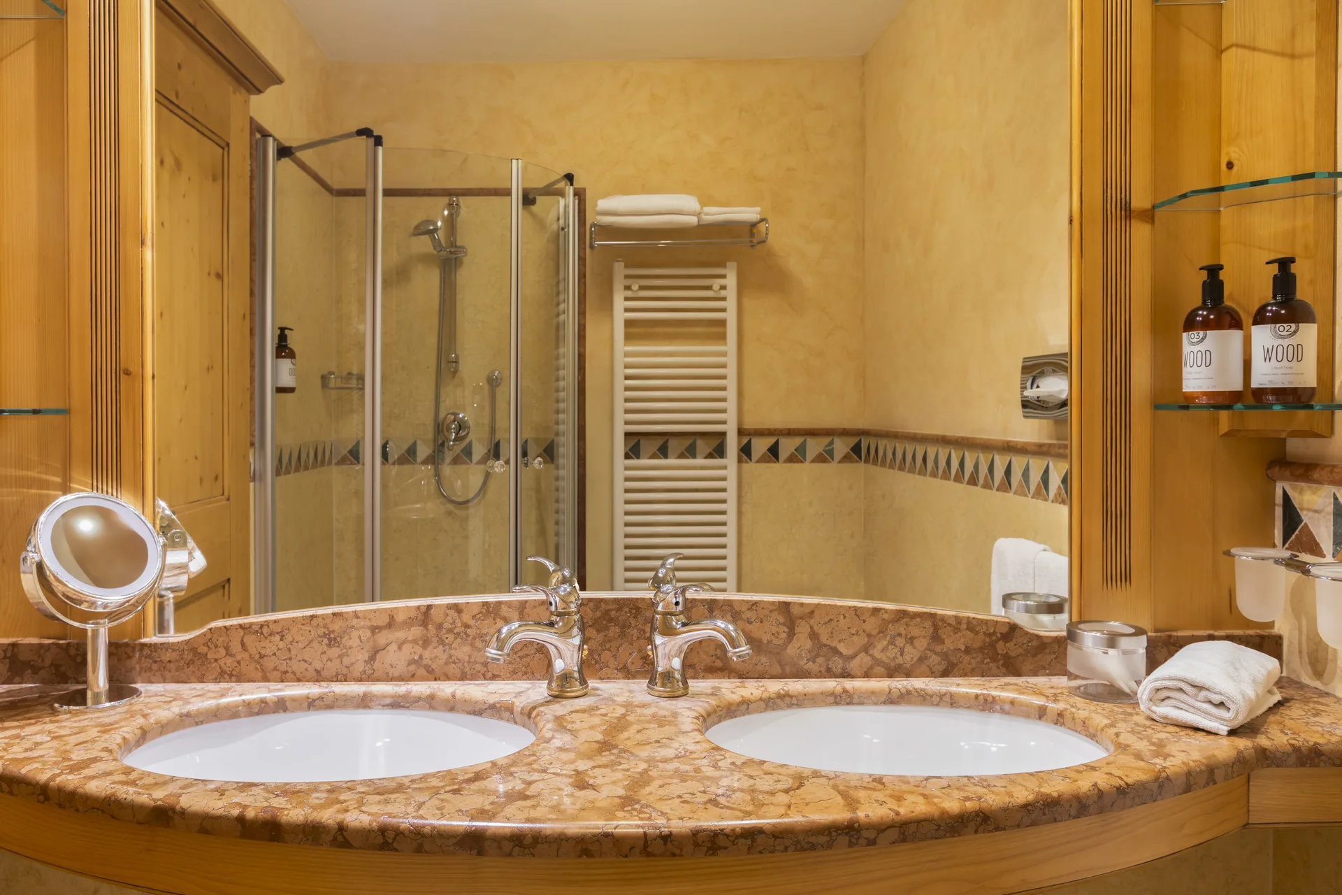 Bagno con doppio lavabo in marmo, doccia in vetro e prodotti da bagno su mensole