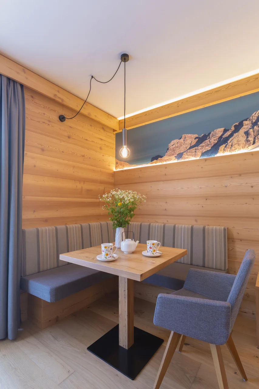 Angolo colazione in camera con panca imbottita, tavolino in legno e stampa delle Dolomiti