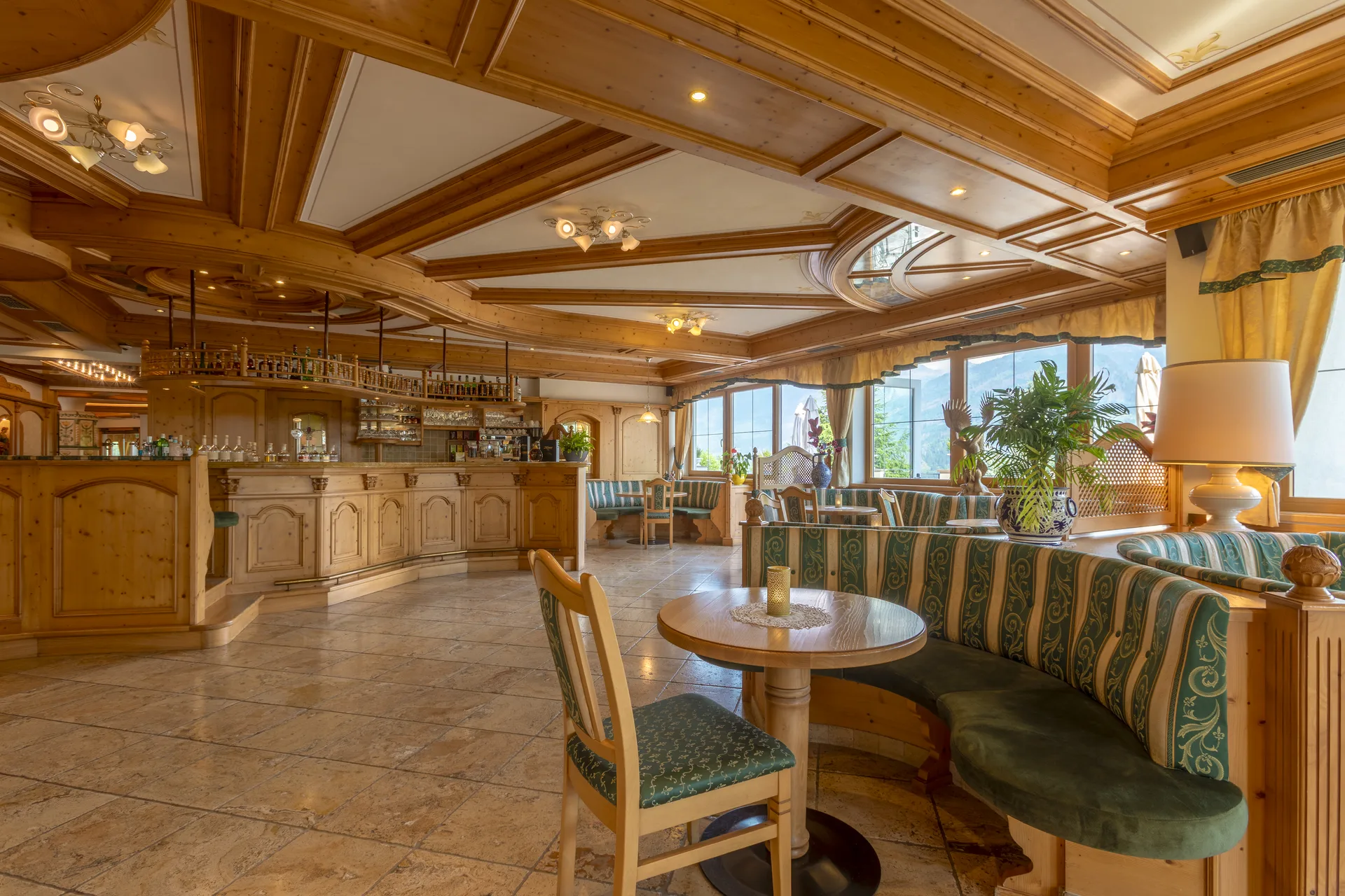 Bar dell'hotel in legno con bancone, divanetti verdi e ampie finestre sulle montagne