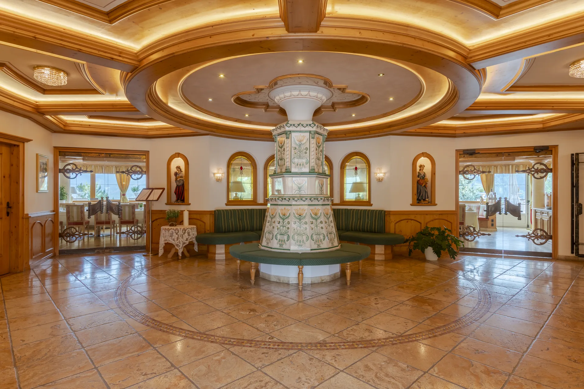 Hall dell'hotel con stufa in maiolica decorata al centro, panche verdi e pavimento in pietra