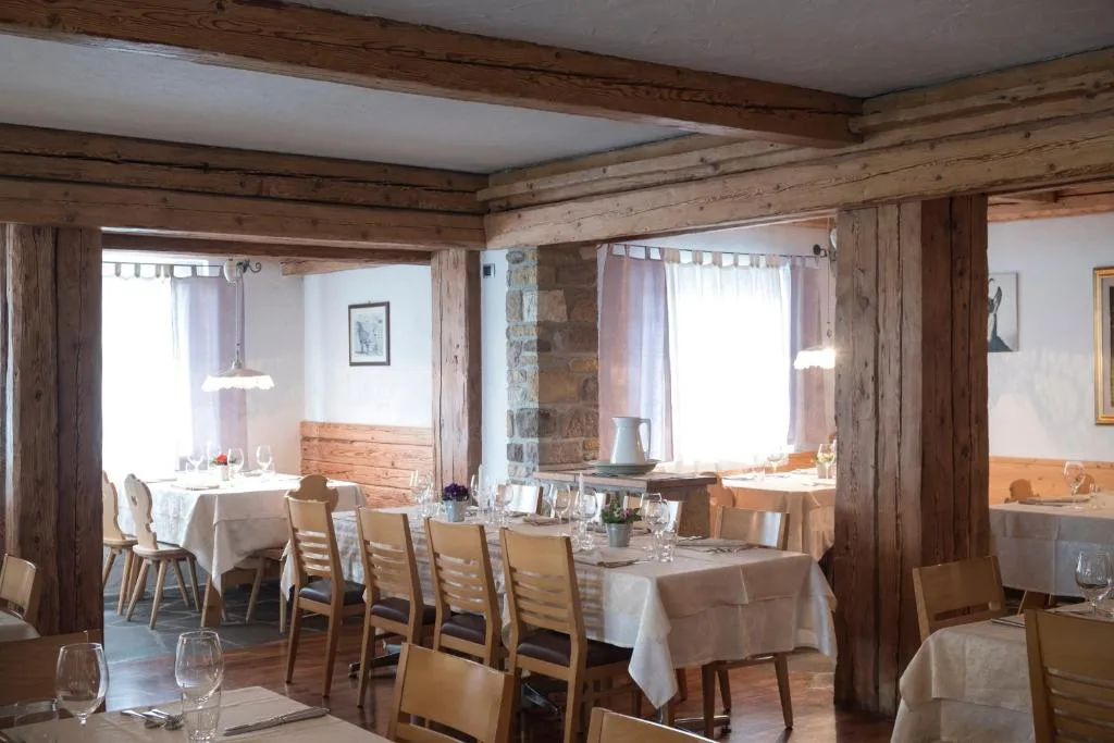Sala da pranzo rustica con travi in legno, tavoli apparecchiati e finestre luminose