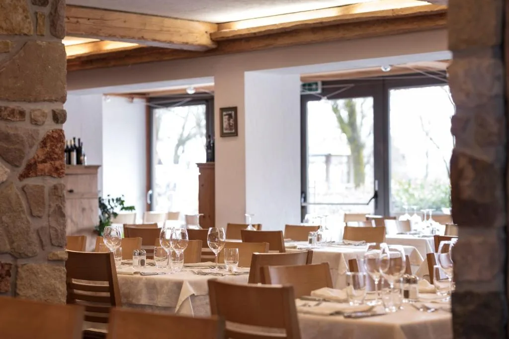 Sala ristorante con tavoli apparecchiati, pareti in pietra e travi in legno
