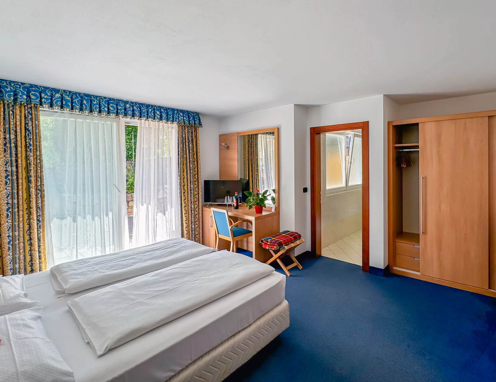 Camera da letto con moquette blu, armadio in legno e accesso al bagno