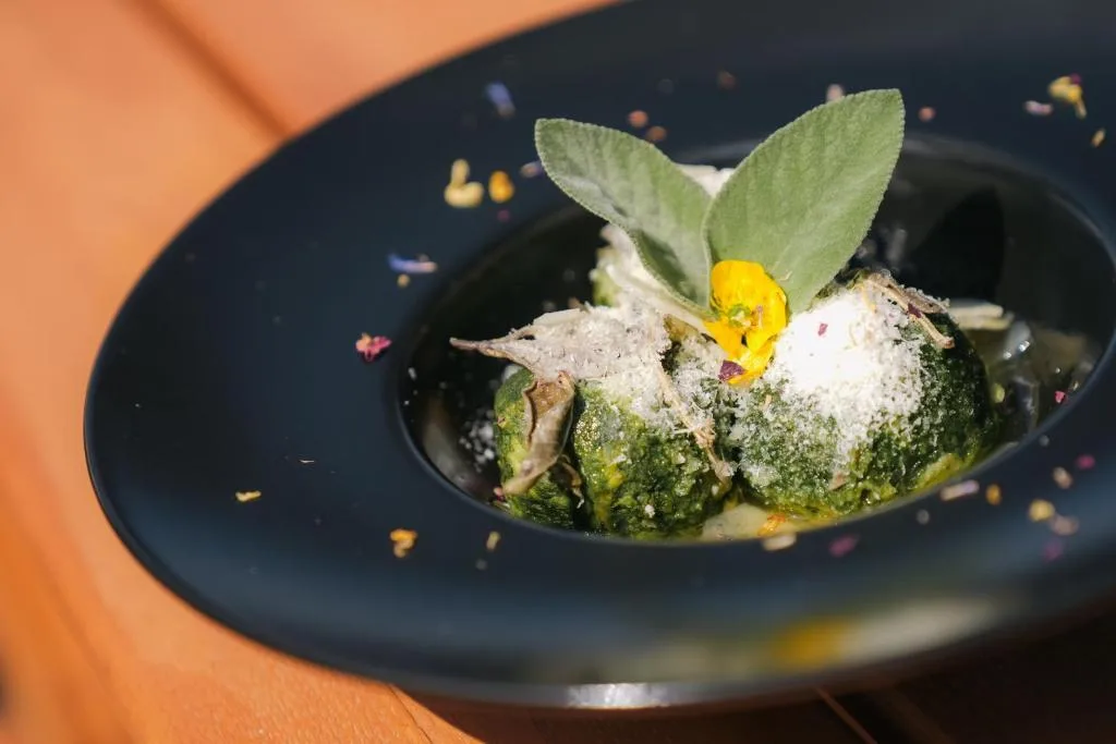 Canederli agli spinaci con formaggio grattugiato e salvia in piatto nero