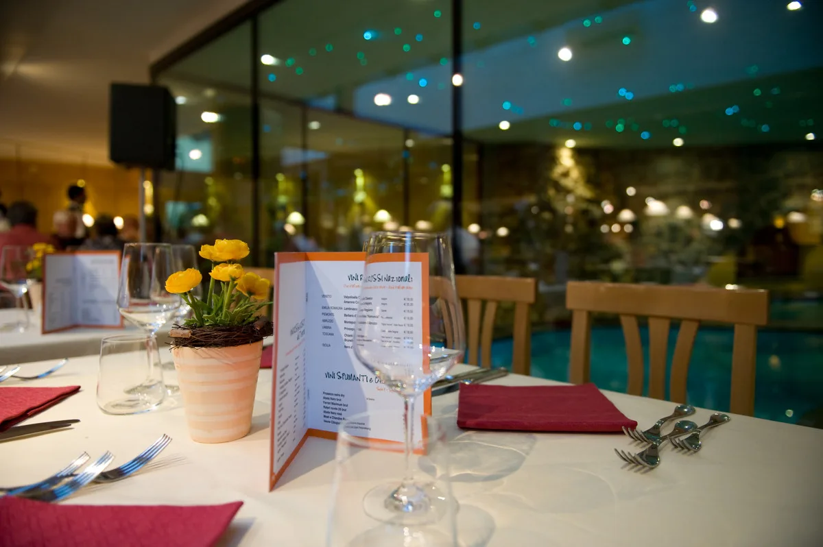 Tavolo del ristorante apparecchiato con menù dei vini e vista sulla piscina