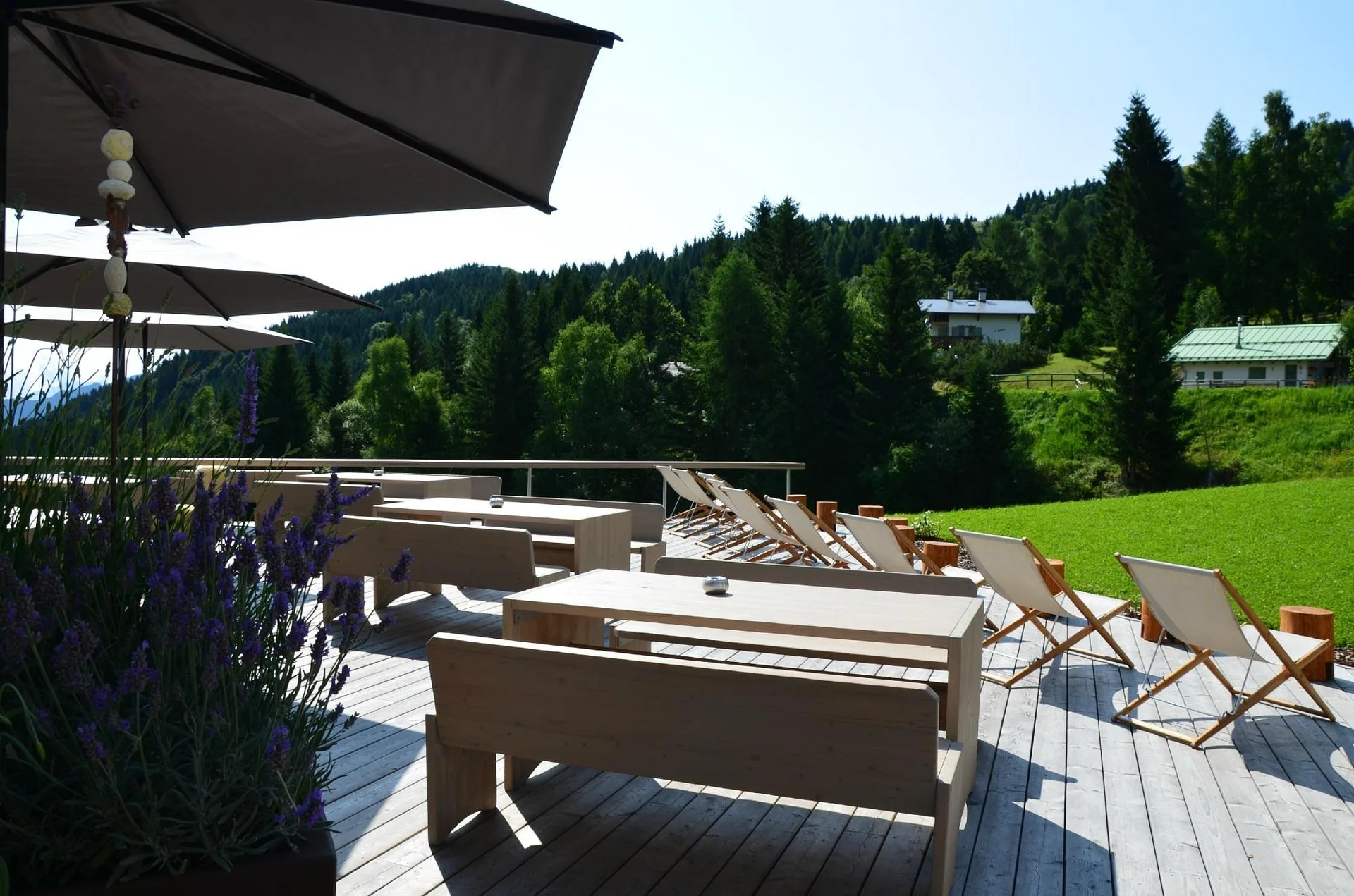 Terrazza estiva con tavoli in legno, sdraio e vista sul bosco