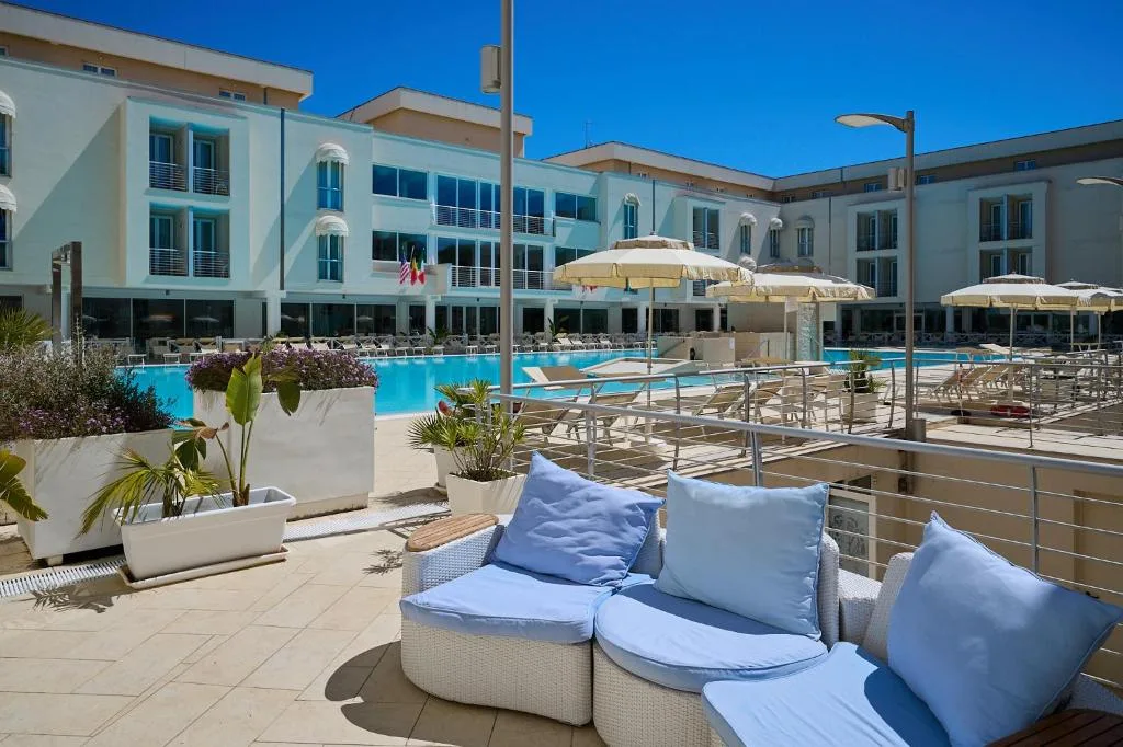 Terrazza con divanetti in rattan e cuscini azzurri affacciata sulla piscina dell'hotel