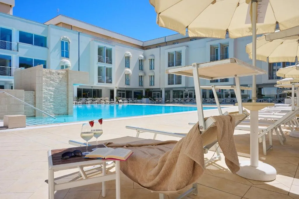 Lettino a bordo piscina con calici di vino, libro e occhiali da sole sotto l'ombrellone