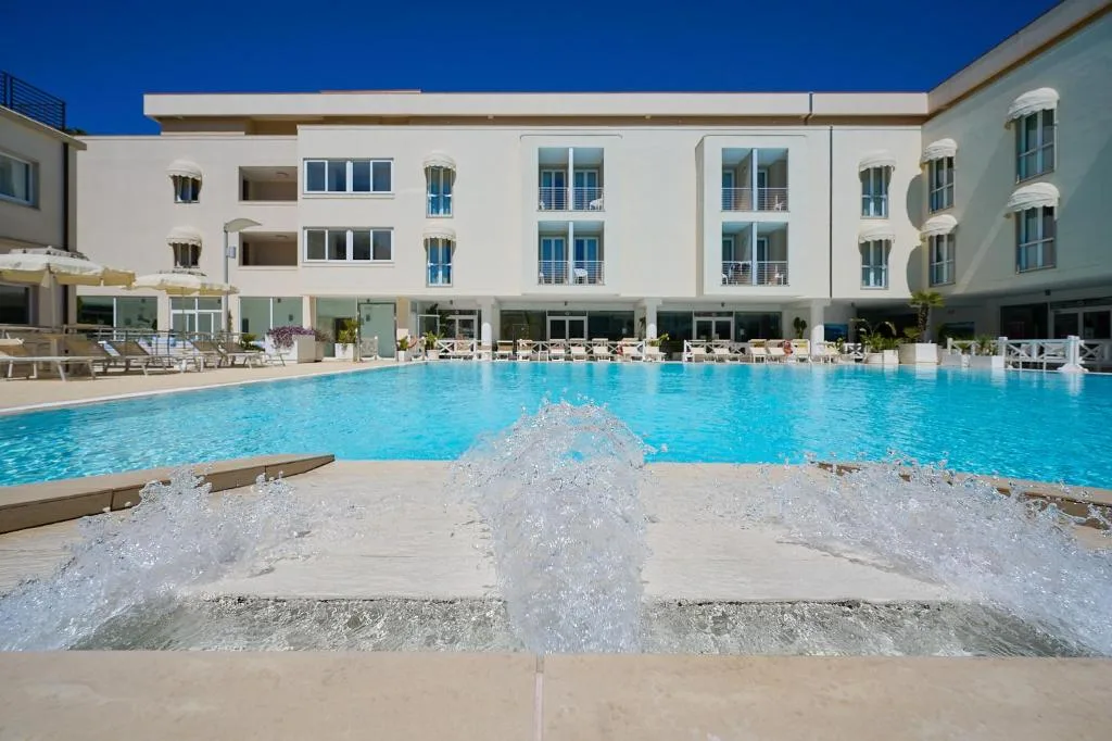 Piscina con giochi d'acqua e cascatelle davanti all'edificio bianco dell'hotel