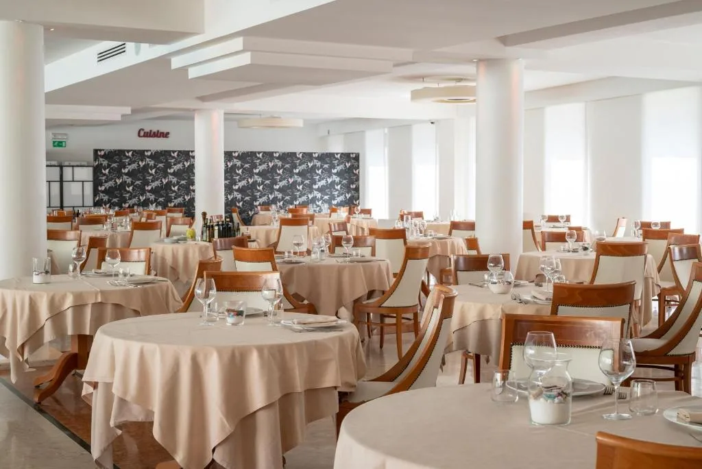 Ampia sala ristorante con colonne bianche, tavoli apparecchiati e parete decorativa