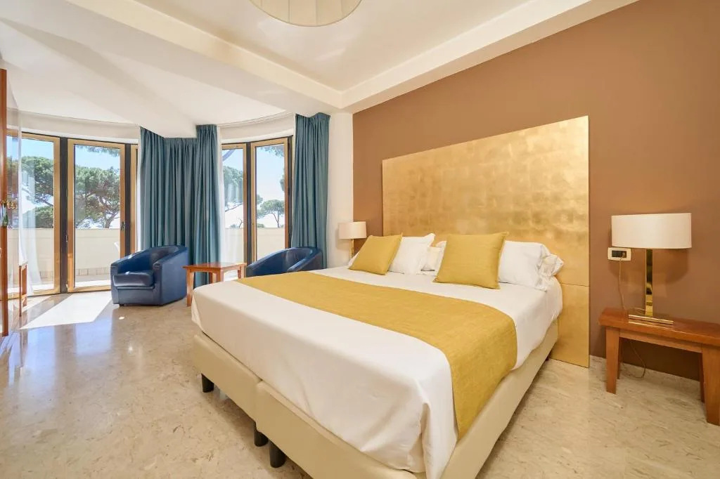 Camera elegante con letto matrimoniale, testiera dorata, poltrone blu e uscita sulla terrazza
