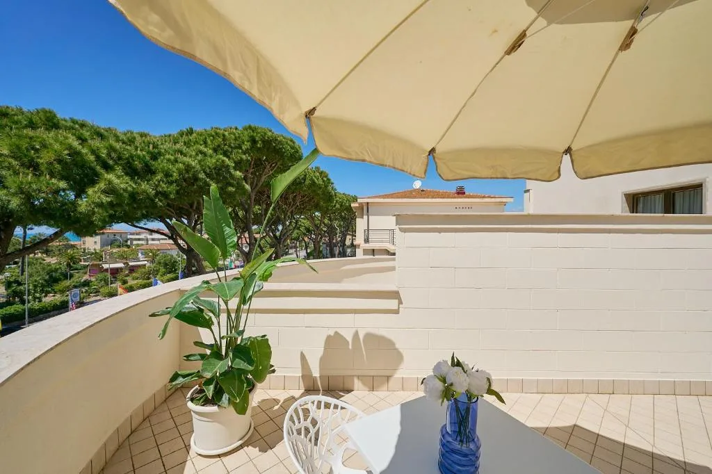 Terrazza privata con ombrellone, tavolino, piante e vista sui pini