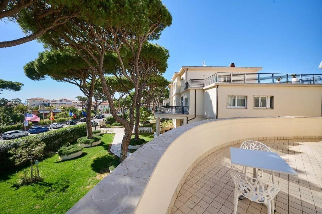 Terrazza panoramica con arredo bianco affacciata sul giardino con pini e bandiere
