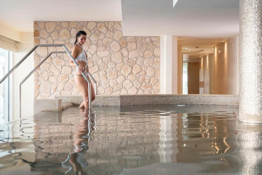 Donna in piscina termale interna con parete in pietra e mosaico