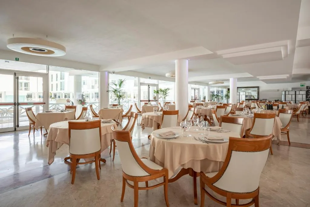 Sala ristorante luminosa con tavoli rotondi apparecchiati e grandi finestre sulla piscina