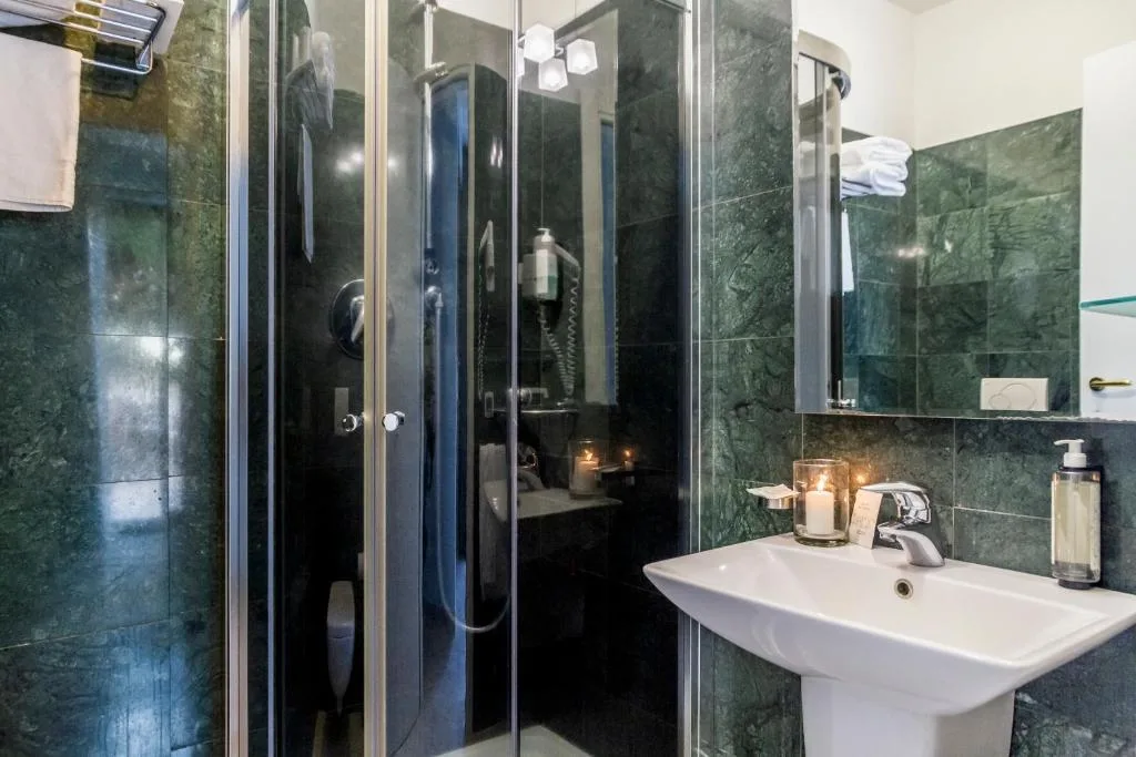 Bagno moderno con marmo verde, doccia in vetro e lavabo bianco con candela