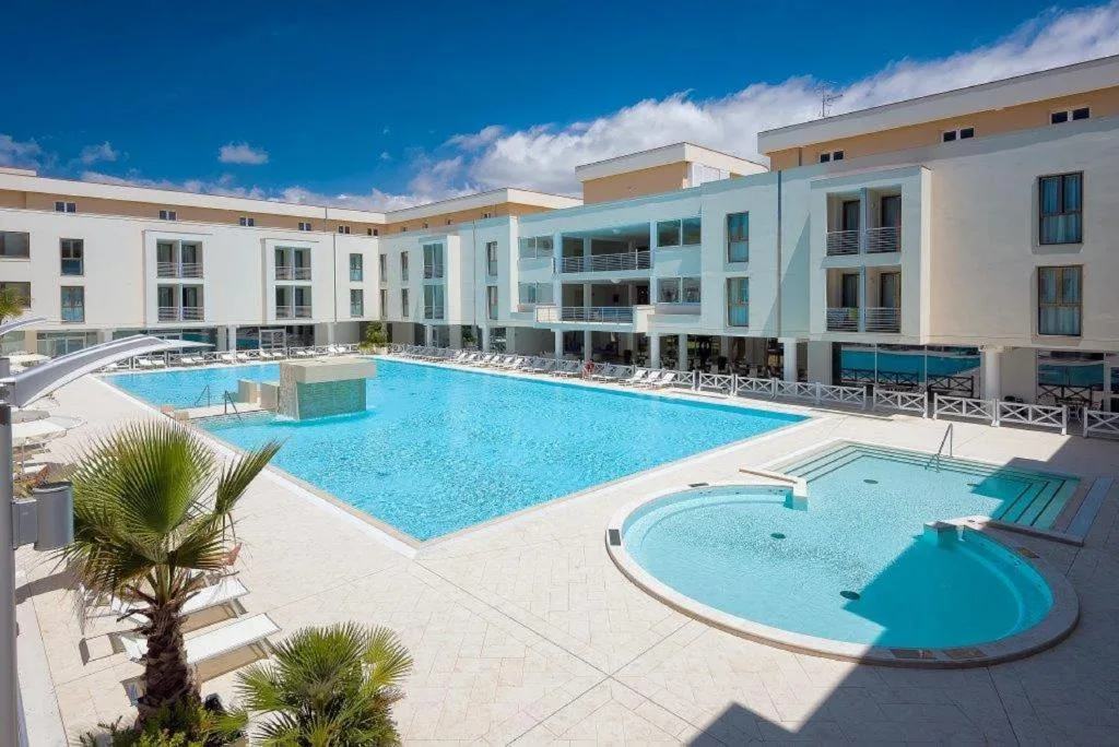 Grande piscina esterna con vasca idromassaggio, lettini e palma sotto il cielo azzurro