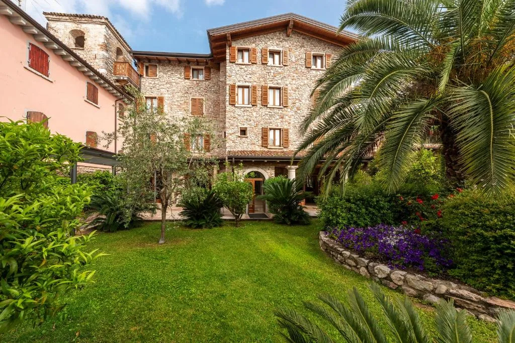 Facciata in pietra dell'hotel con giardino curato, palme e fioriture colorate