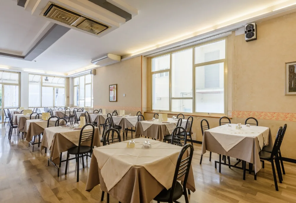 Sala ristorante con tavoli apparecchiati con tovaglie beige e grandi finestre