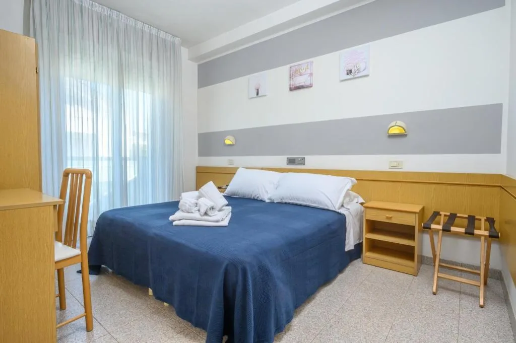 Camera con letto matrimoniale, copriletto blu, scrivania e ampia finestra