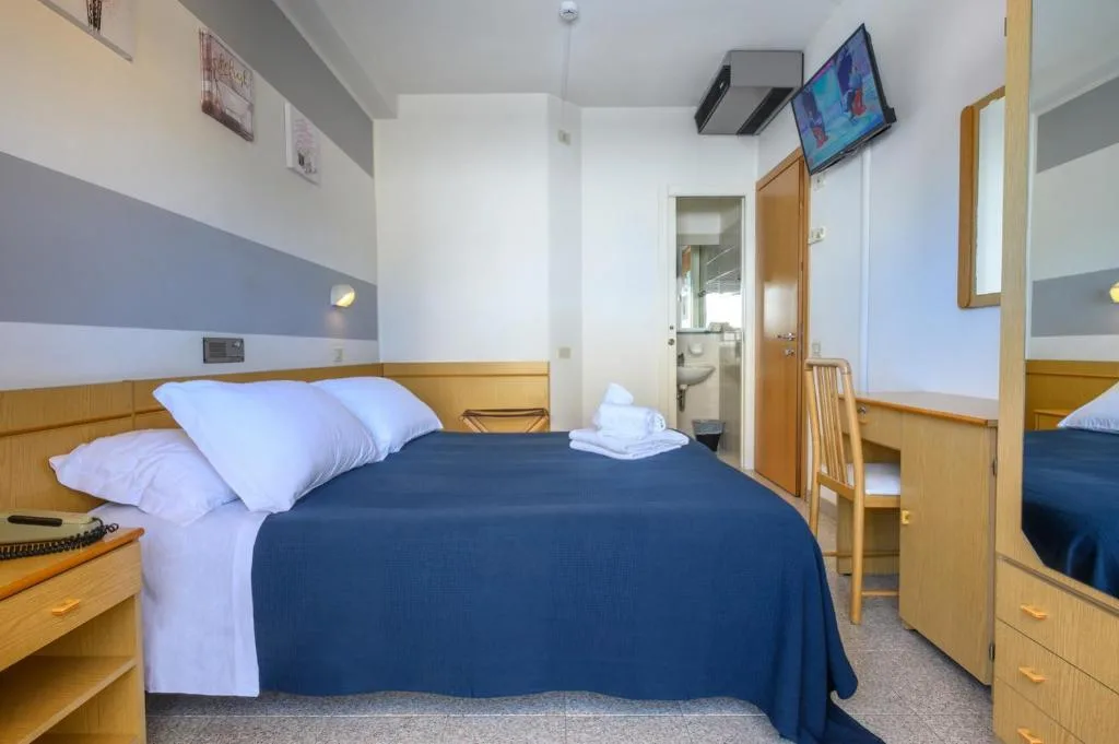 Camera con letto matrimoniale, copriletto blu, TV, scrivania e bagno privato