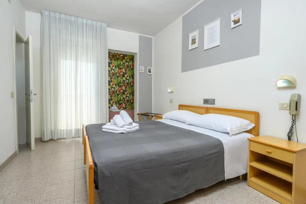 Camera matrimoniale con copriletto grigio, telefono e dettaglio floreale a parete