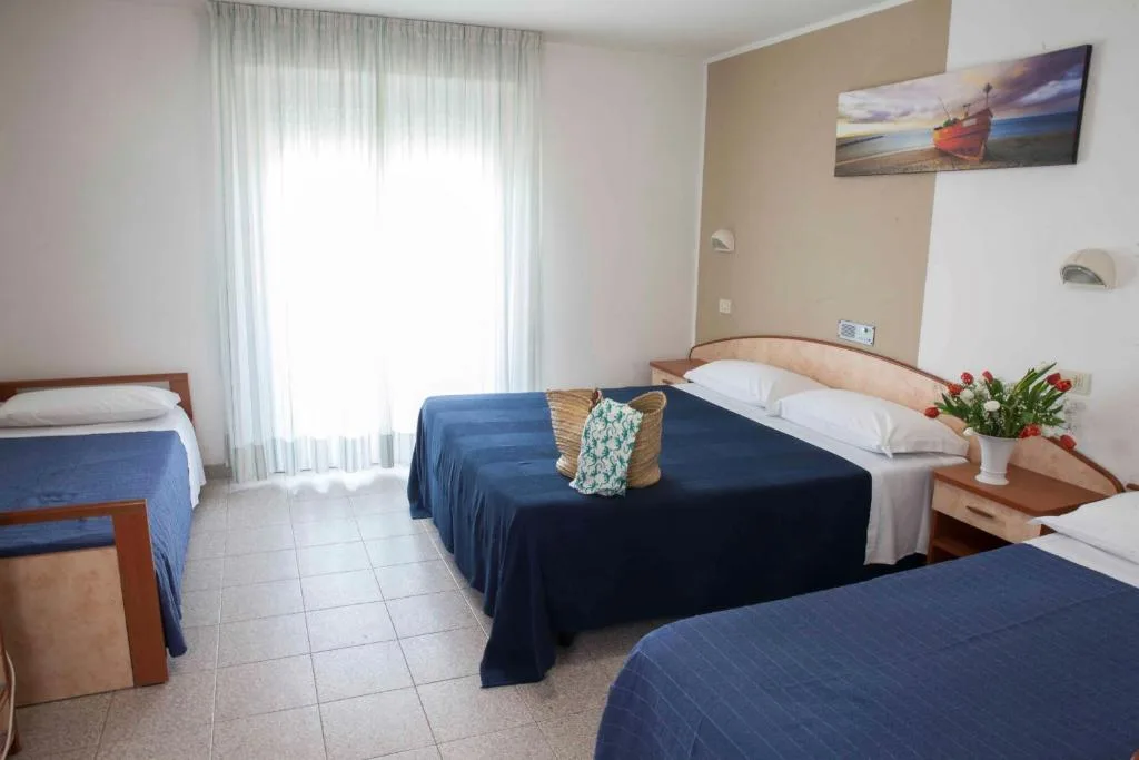 Camera tripla con letto matrimoniale e singolo, copriletti blu e finestra luminosa