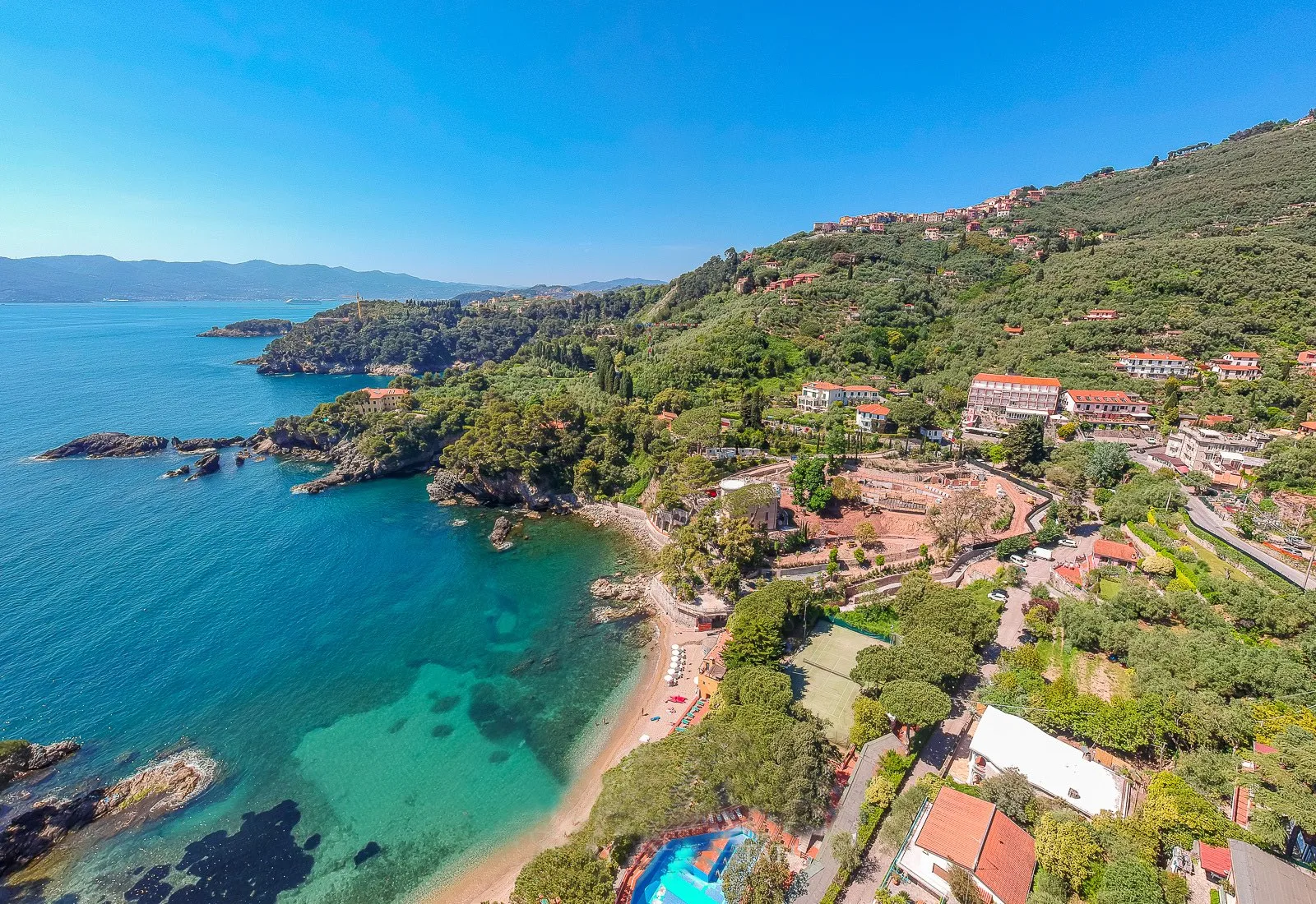 Panorama aereo della costa con calette, spiaggia sabbiosa, piscina e colline coltivate a olivi