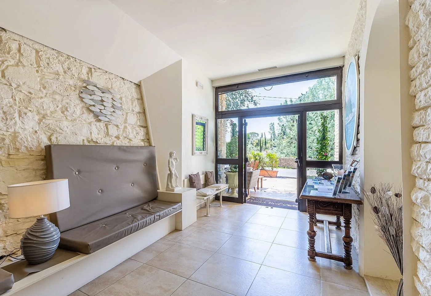 Ingresso dell'hotel con pareti in pietra, divano imbottito e porta a vetri sul giardino