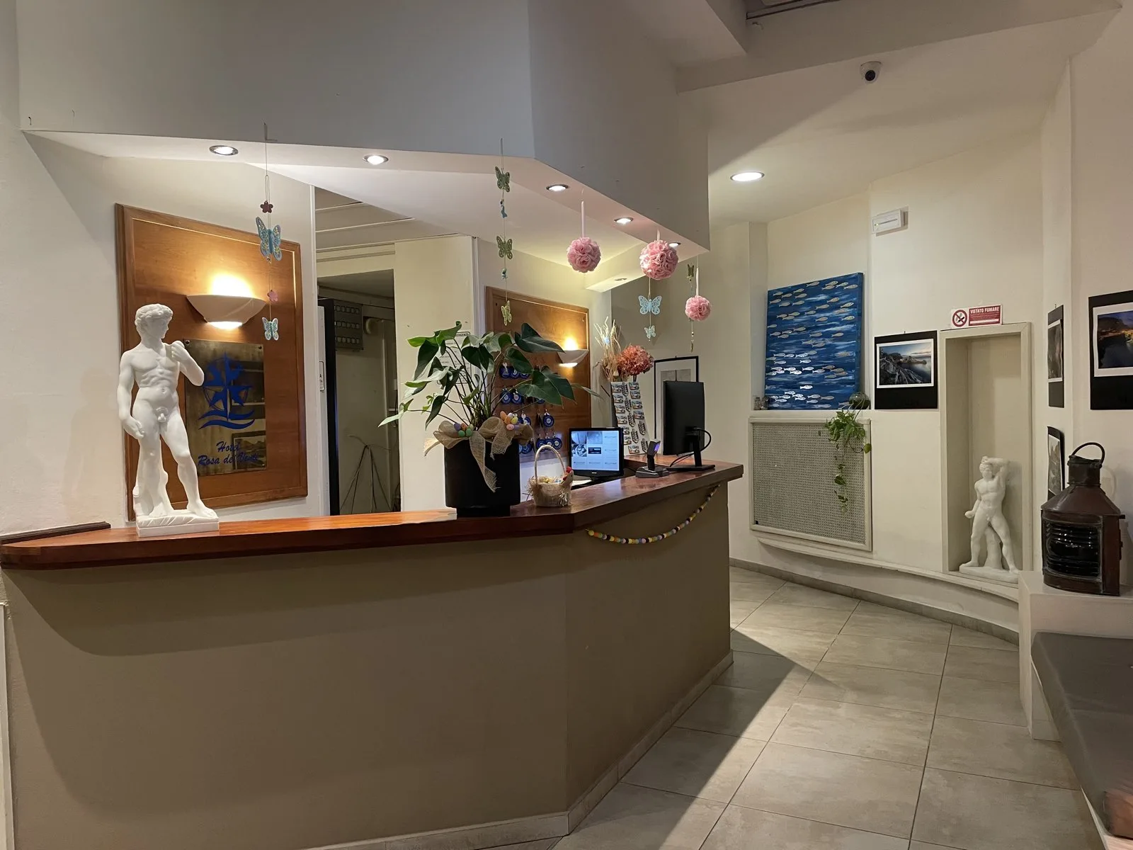 Banco della reception dell'hotel con statua decorativa, monitor e decorazioni floreali