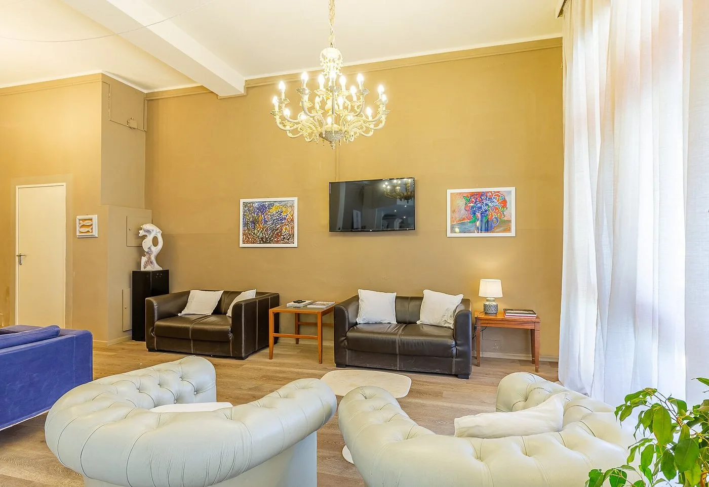 Area lounge con divani in pelle, poltrone chesterfield, lampadario in vetro e TV a parete