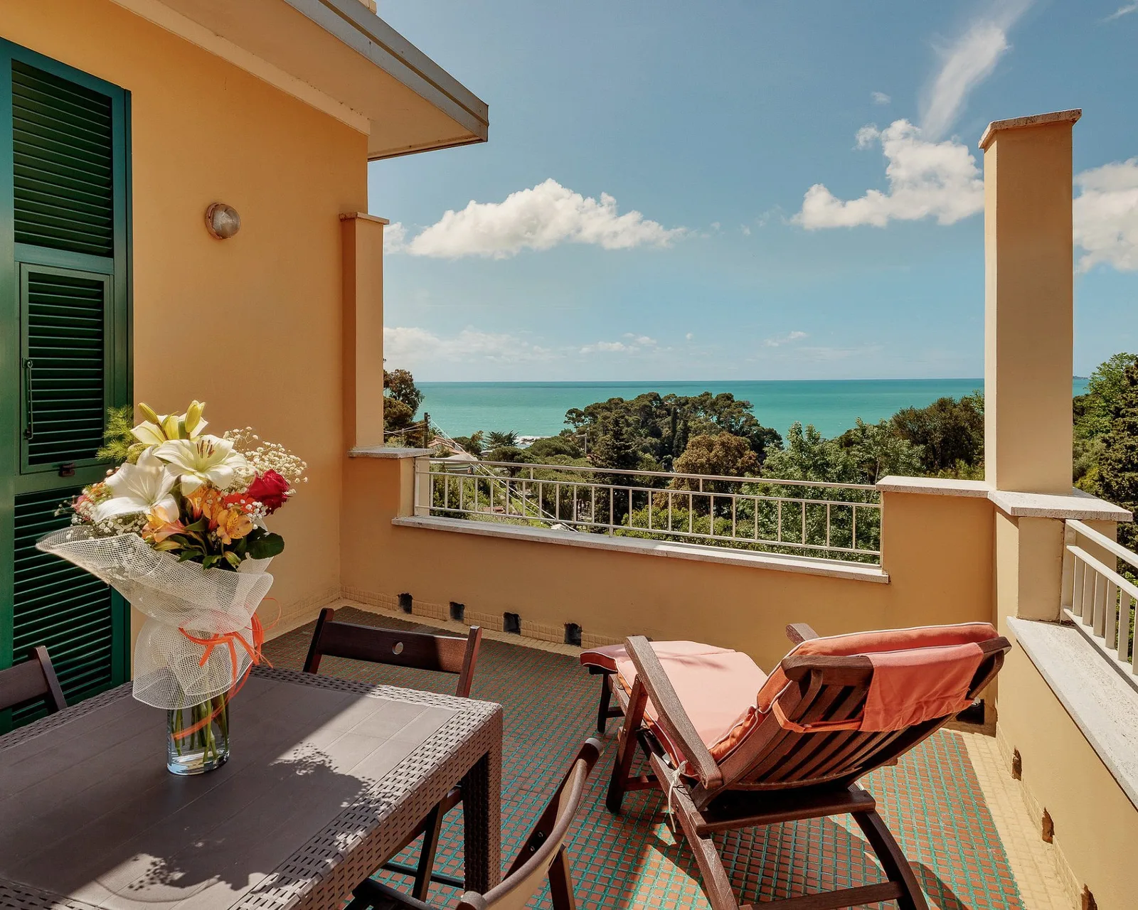 Balcone con tavolo, sedie e lettino affacciato sul mare e sulla vegetazione