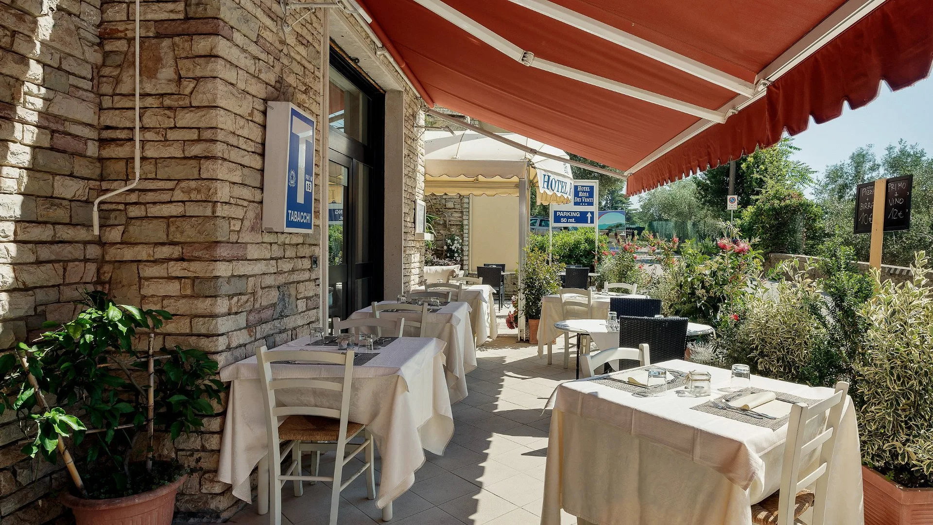 Terrazza esterna del ristorante con tavoli apparecchiati, tende rosse e pareti in pietra