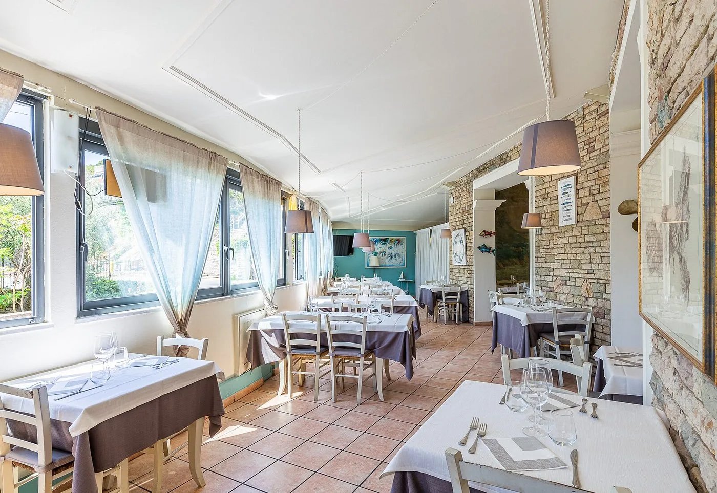 Sala interna del ristorante con tavoli apparecchiati, pareti in pietra e finestre luminose
