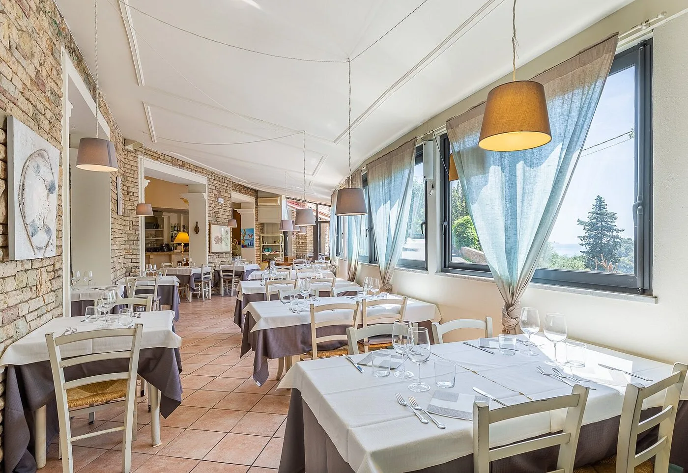 Sala ristorante luminosa con tavoli apparecchiati, lampade a sospensione e vista sul verde