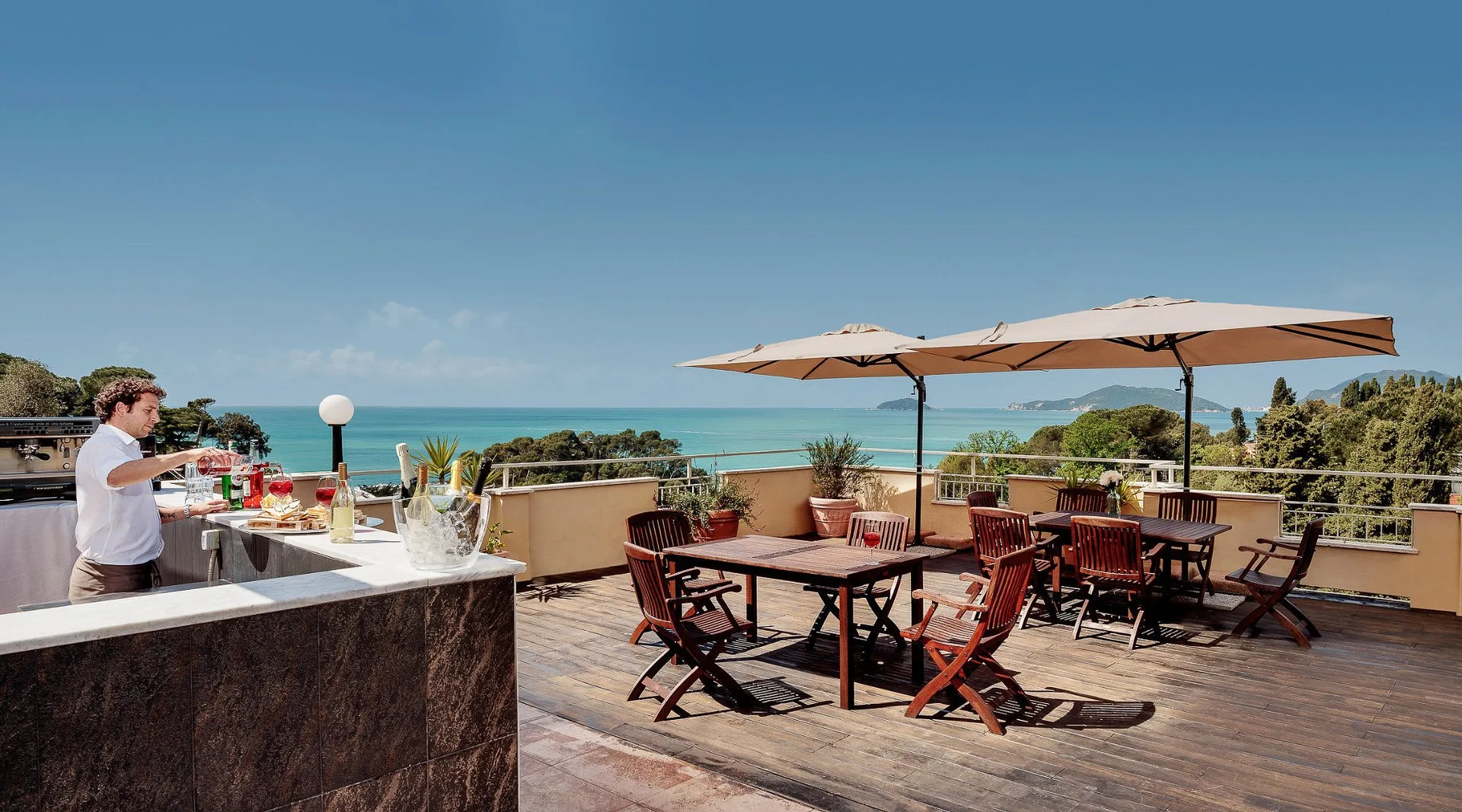 Terrazza bar con cameriere, tavoli sotto gli ombrelloni e vista mozzafiato sul golfo