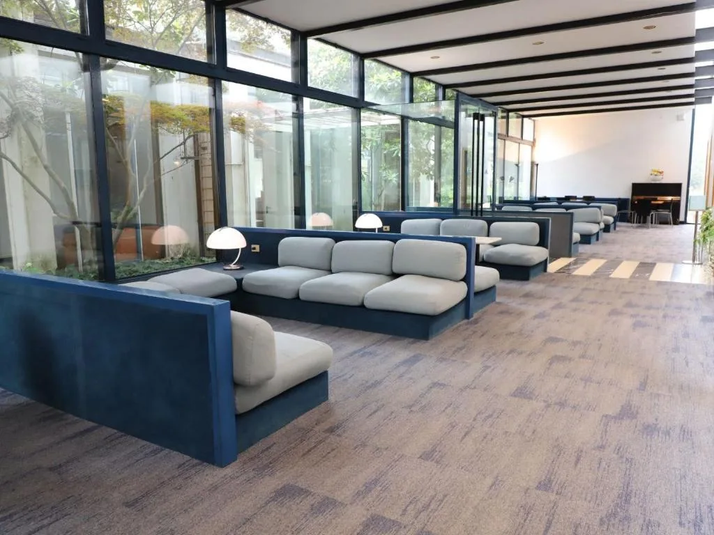 Area lounge con divani grigi lungo grandi vetrate affacciate su un giardino interno