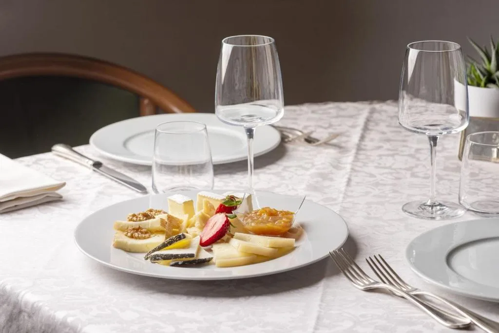 Tavola apparecchiata con piatto di formaggi, noci e composta e bicchieri di vino