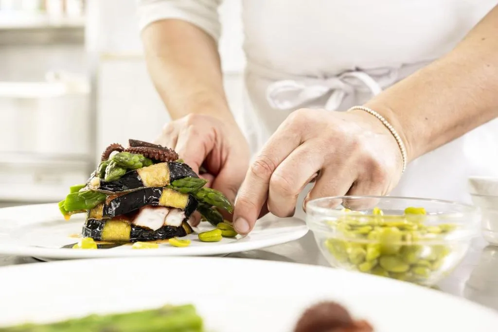 Chef impiatta un piatto gourmet con verdure, asparagi e polpo in cucina
