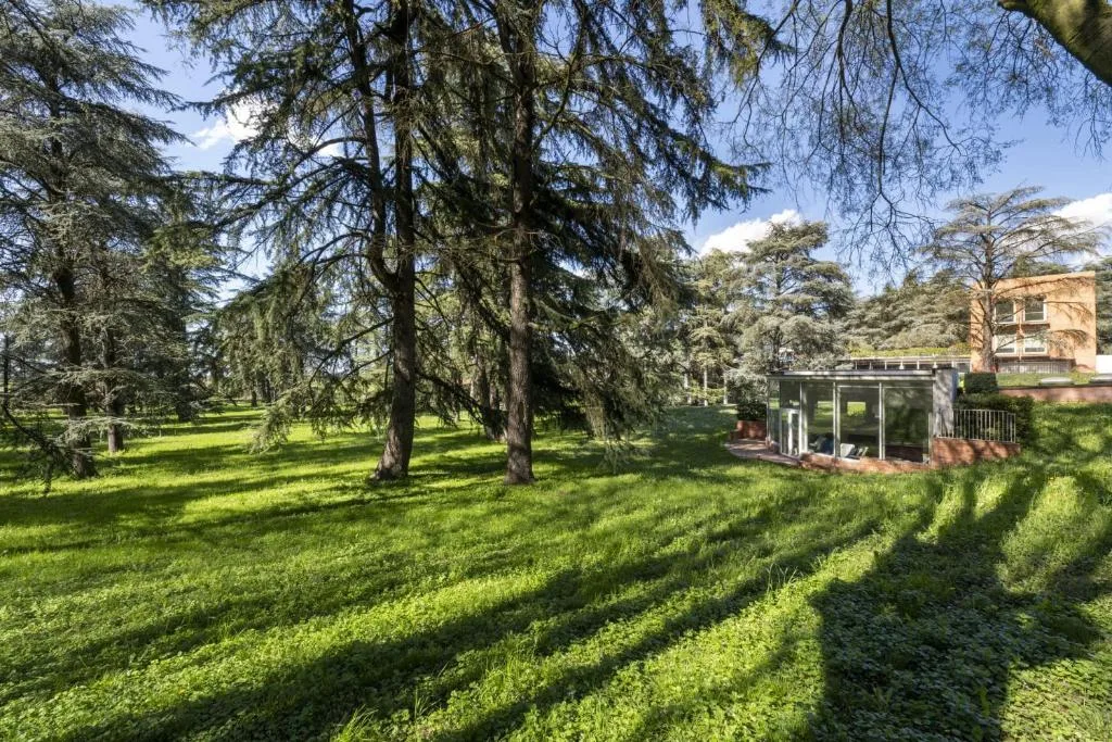 Ampio parco verde con alberi secolari e struttura vetrata dell'hotel