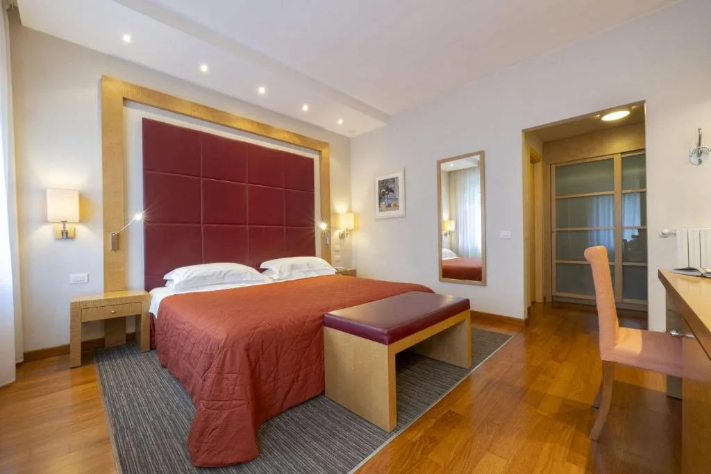 Camera matrimoniale con testiera rossa, pavimento in parquet, scrivania e specchio