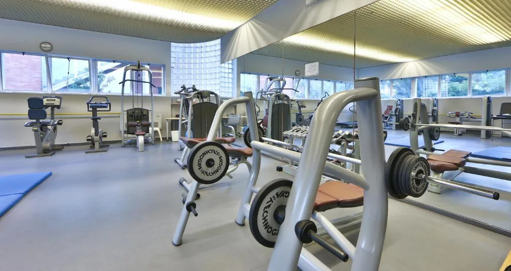 Palestra attrezzata con macchinari, pesi e cyclette illuminata da grandi finestre