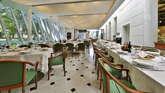 Sala ristorante con tavoli apparecchiati, sedie verdi e pavimento in marmo a fianco delle vetrate