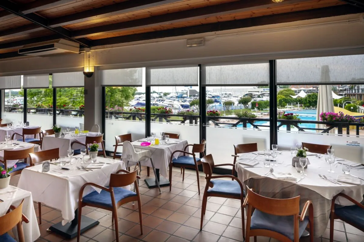 Sala ristorante con tavoli apparecchiati e vista sul porto
