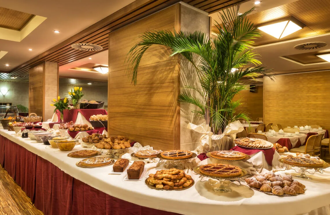 Buffet della colazione con crostate, cornetti e dolci disposti su tavolo decorato con palme